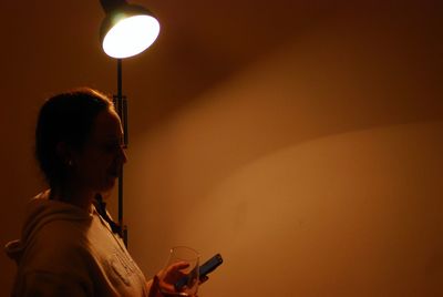 Woman using mobile phone by lamp at home