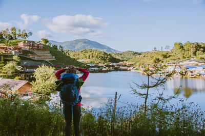 Rear view of woman standing by lake against sky