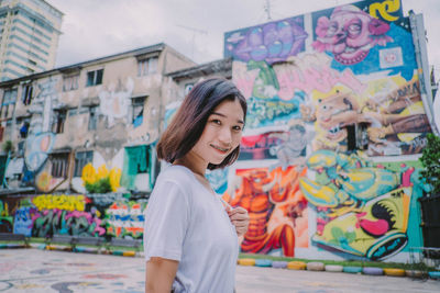 Portrait of smiling young woman standing against graffiti wall