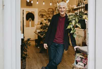 Portrait of happy senior male owner leaning on table at store