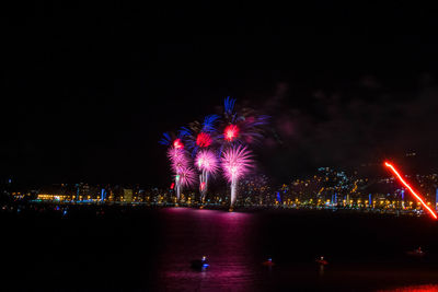 Firework display over illuminated city against sky at night