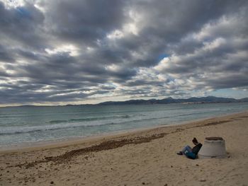 Man sitting on shore at beach against sky