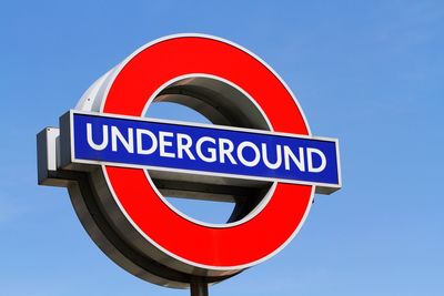 Low angle view of london underground sign against blue sky