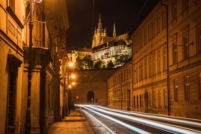 Illuminated light trails on road amidst buildings in city at night