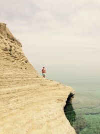 Man on cliff on beach against sky