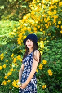 Portrait of a smiling young woman standing on yellow flowering plants