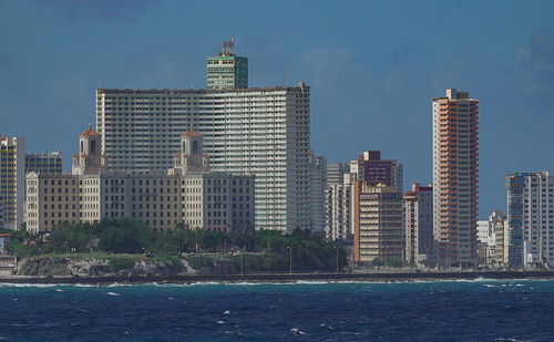 Modern cityscape by sea against sky