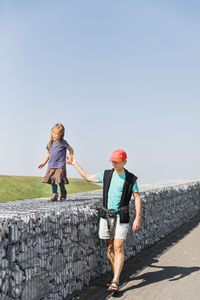 Full length of grandfather with granddaughter walking against clear sky