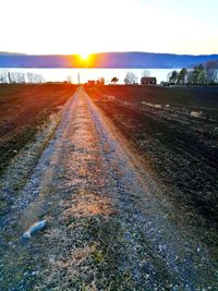 Road amidst field against sky during sunset