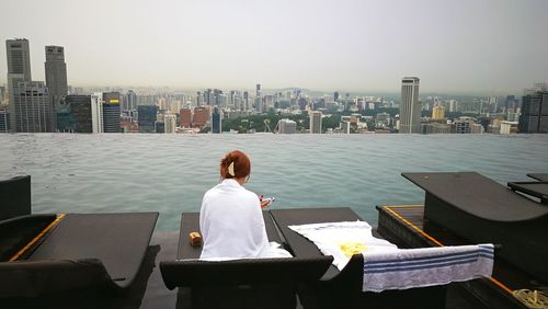 Rear view of teenager sitting at tourist resort against cityscape