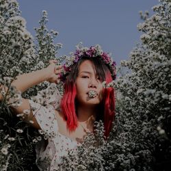 Portrait of beautiful woman standing by flowering plants against clear sky