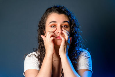 Young woman with black hair with both hands on her face. looking at the camera. 