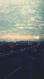 Cars on road against cloudy sky at sunset