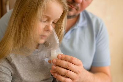 Dad helps his sick child do inhalation with a nebulizer at home. he holds a mask from which steam