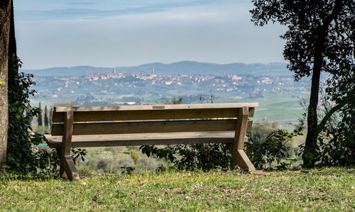Empty bench on field against sky
