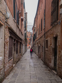 Rear view of woman walking on footpath amidst buildings in city