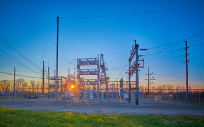 Electricity pylons against clear blue sky during sunset