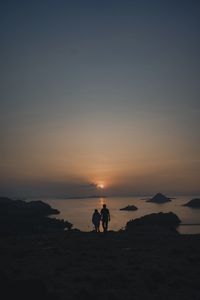 Silhouette of people on beach against sky during sunset