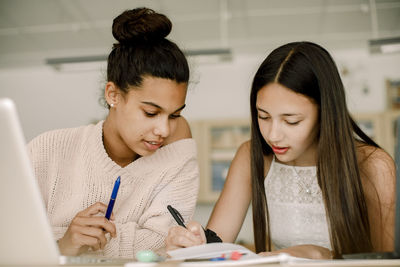 Female teenagers studying while sitting by table in classroom