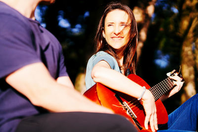 Woman playing guitar by man against trees