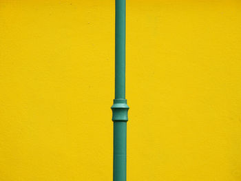 Close-up of green pole against yellow wall