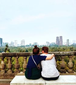 Rear view of man and woman sitting against sky in city