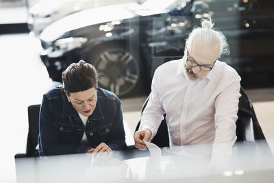 Senior man and woman reading documents while sitting at car showroom