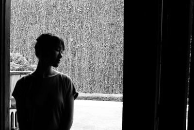 Young woman looking away while standing by window at home