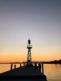 Silhouette lighthouse by sea against sky during sunset