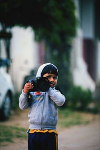 Portrait of boy holding camera on street