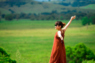 Young woman wearing sunglasses with arms outstretched standing on landscape