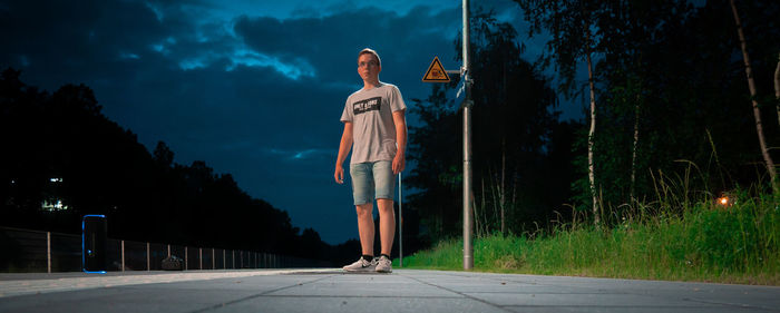 Man standing by illuminated road against sky at night