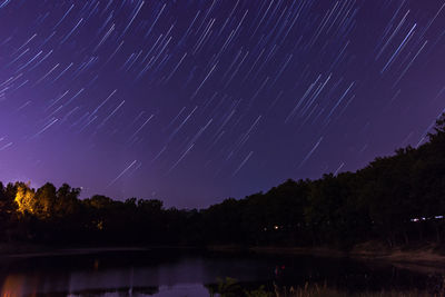 Low angle view of trees by lake against sky at night