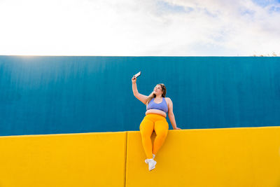 Low angle view of woman taking selfie sitting on wall