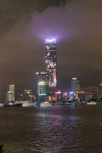 Illuminated buildings by sea against sky at night