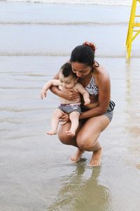 Mother carrying daughter while crouching in sea