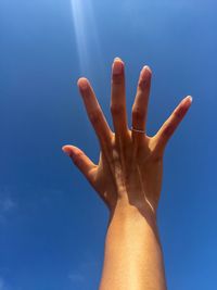 Cropped hand of woman reaching blue sky
