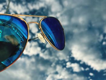 Close-up of sunglasses against cloudy sky