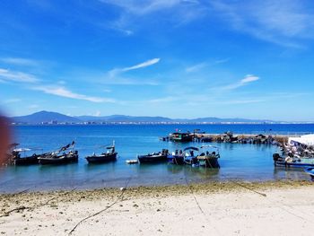 Boats moored at harbor against blue sky