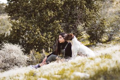 Teenage girl with dog sitting on grassy field at park