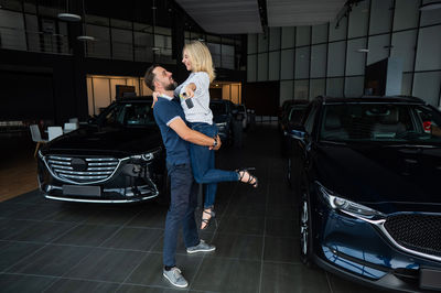 Happy caucasian couple hugging while buying a new car in a car dealership