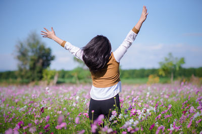 Rear view of woman with arms raised standing on flowering field