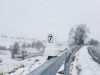 Road by snow covered landscape against clear sky