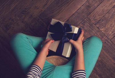 Low section of girl holding gift box while sitting on hardwood floor