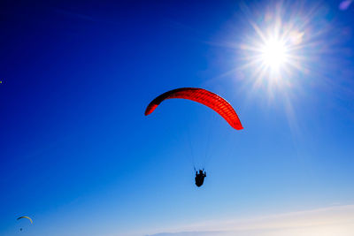 Paragliding above mountain peaks and white clouds during winter blue sunny day.