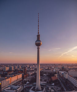 Communications tower in city against sky during sunset