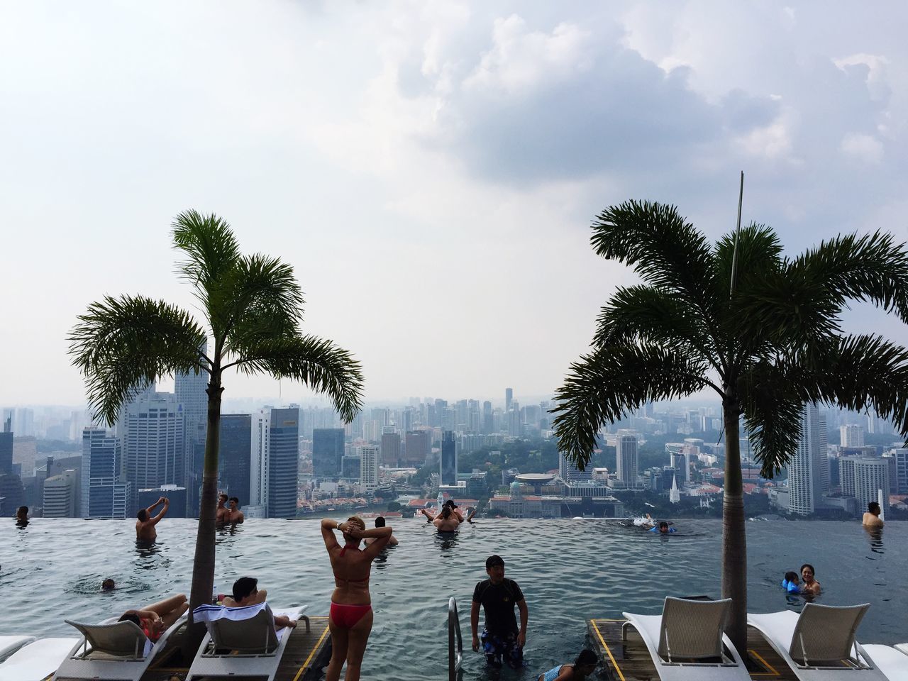 water, tree, lifestyles, large group of people, men, leisure activity, sky, person, city, building exterior, city life, mixed age range, cloud - sky, nautical vessel, sitting, sea, day, beach, built structure