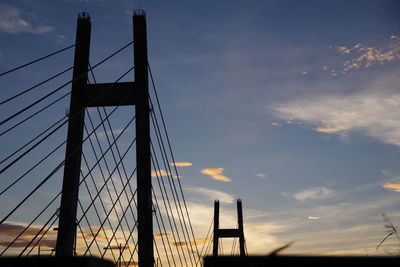 Low angle view of suspension bridge against cloudy sky