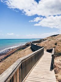 Boardwalk on cliff by sea against sky