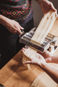 Cropped image of women preparing pasta with machine in kitchen